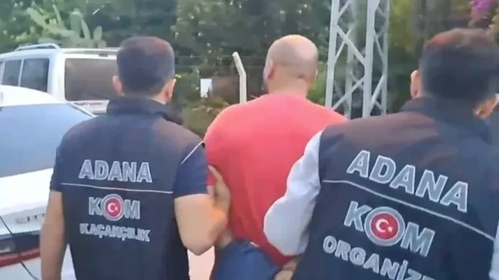 Adana KOM ekipleri, gözaltındaki bir şüpheliyi araçların bulunduğu alanda götürüyor.
