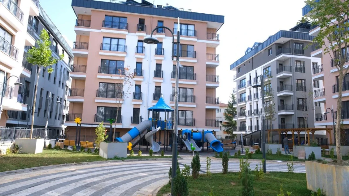Apartman bloklarının arasında çocuk oyun alanı ve peyzaj bulunan konut sitesi