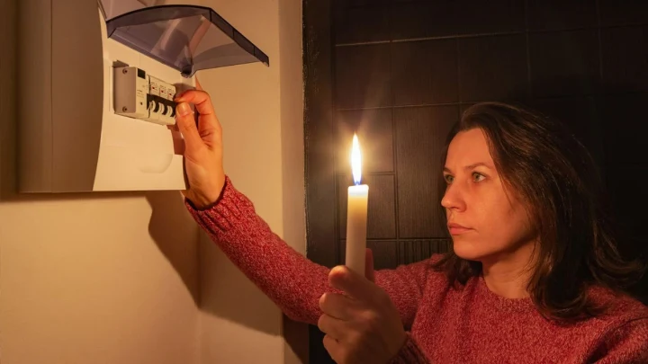 Elektrik kesintisi sırasında elinde mum tutan bir kadın, elektrik panosundaki sigortayı kontrol ediyor.