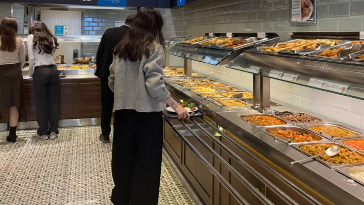 Bir öğrenci yemek tezgâhındaki yemekleri inceliyor