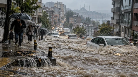 Şiddetli yağışın ardından bir kent caddesinde sel suları araçları ve kaldırımı kaplıyor.