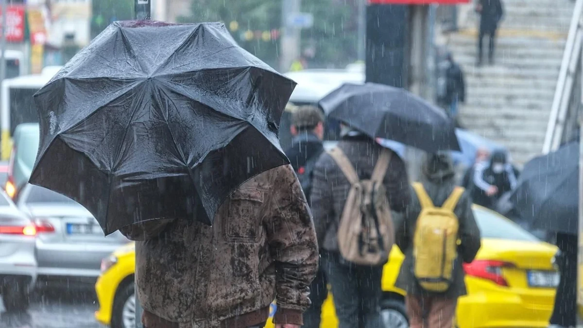 Yağmur altında şemsiyeyle yürüyen yayalar ve trafikte araçlar