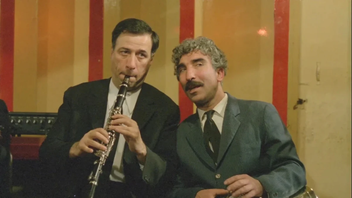 Köyden İndim Şehire filminden bir sahnede iki oyuncu; oyunculardan biri klarnet çalıyor.