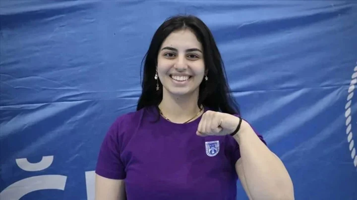 Milli bilek güreşi sporcusu Azra Sarı, mor tişörtüyle kameraya gülümsüyor.