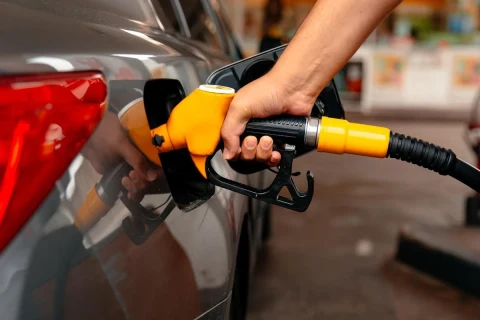 Bir kişi, sarı renkli yakıt pompasıyla otomobilin deposuna benzin dolduruyor.