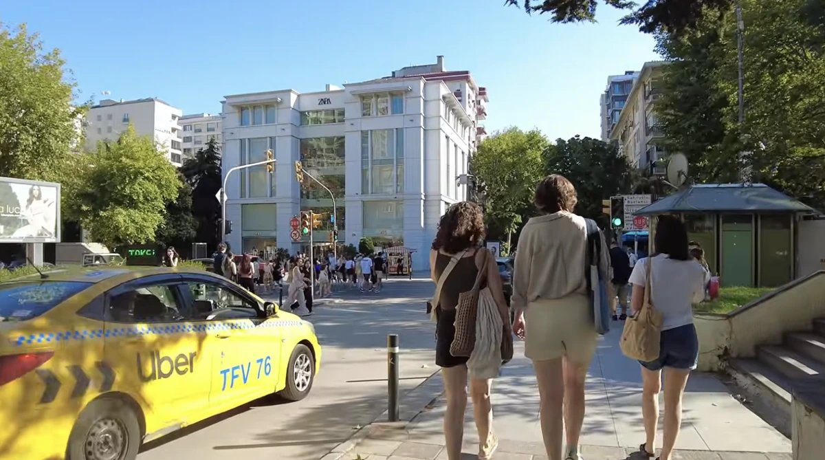 Bir caddede yürüyen yayalar ve yol kenarındaki sarı taksi