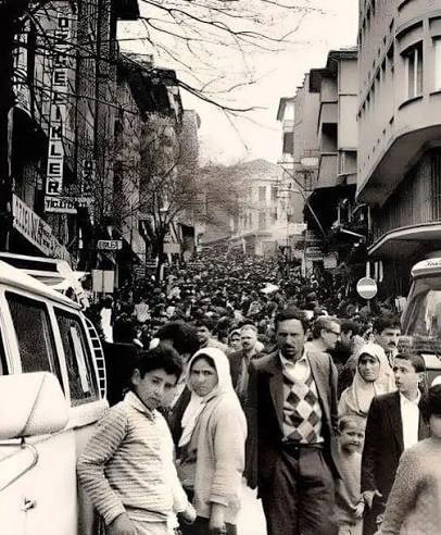 Kalabalık bir caddede yürüyen insanlar ve dükkânlar