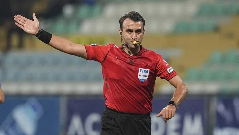 Kırmızı formasıyla sahada düdük çalan futbol hakemi
