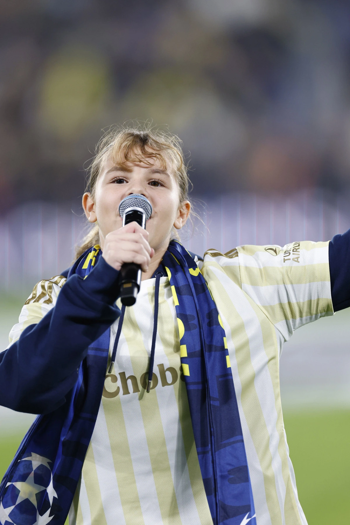 Eliz Dağdağan, Fenerbahçe forması ve atkısıyla mikrofonla marş söylüyor