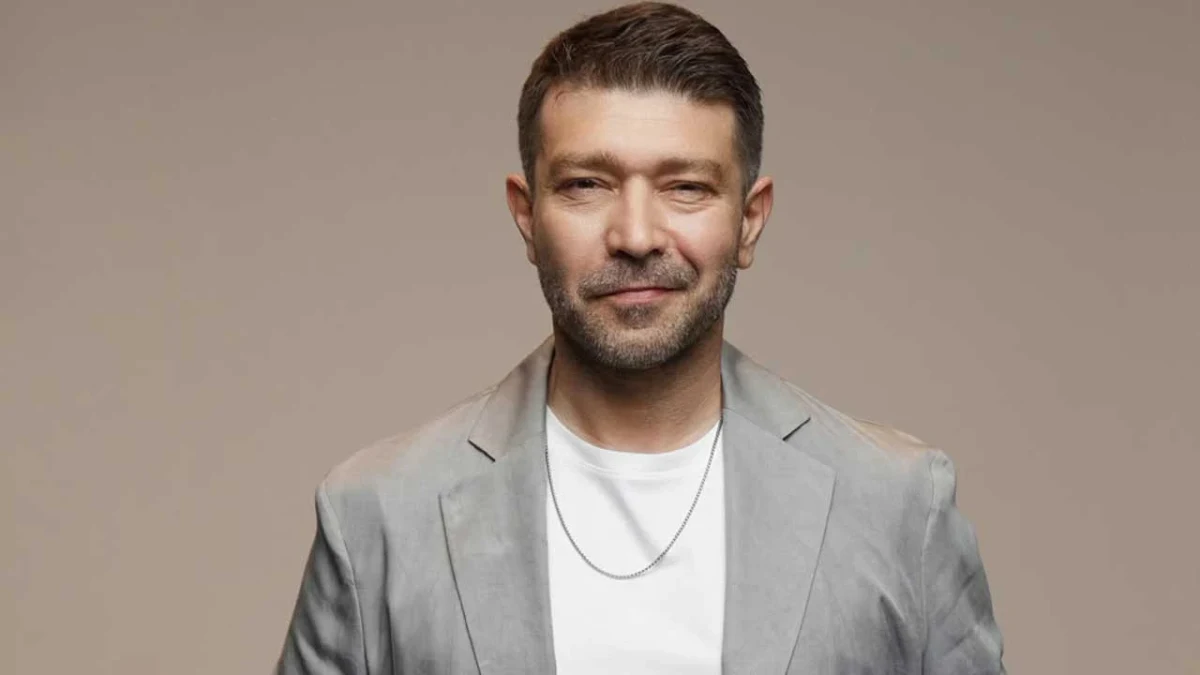 Emre Başer, gri takım elbiseyle kameraya bakıyor