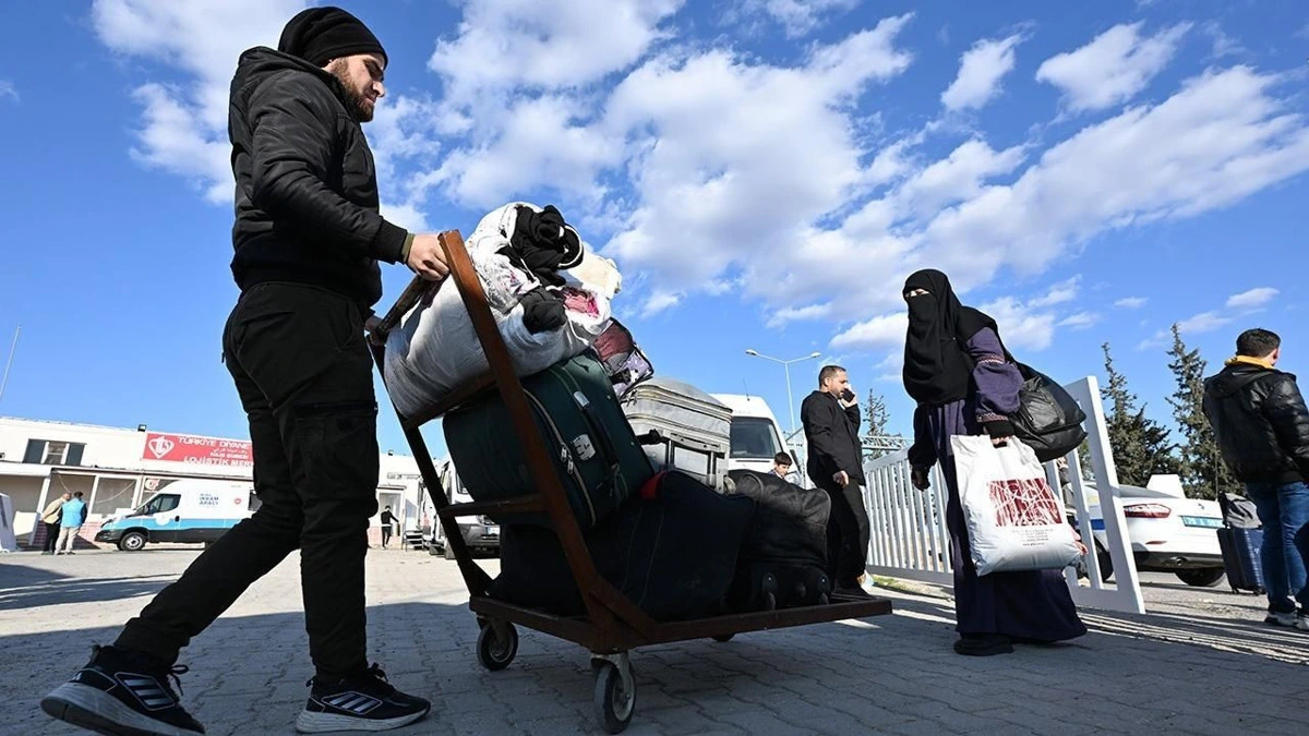 Eşyalar yüklü el arabasını iten bir kişi ve yanında bavul taşıyan insanlar