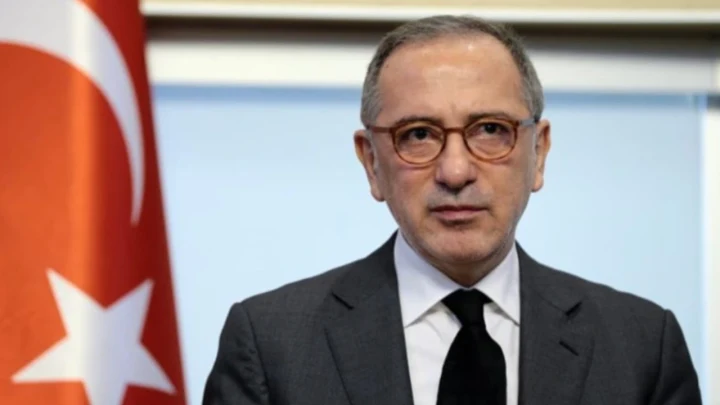 Fatih Altaylı, Türk bayrağının önünde takım elbiseyle kameraya bakıyor.
