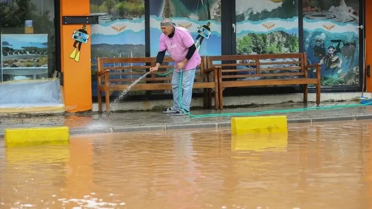 Fethiye’de sağanak sonrası suyla kaplanan bir sokak ve kaldırımda temizlik yapan kişi