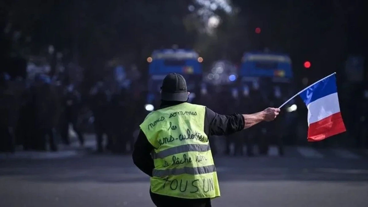 Sarı yelekli bir kişi elinde Fransa bayrağı tutuyor
