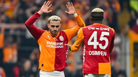 Galatasaray forması giyen iki futbolcu maç sırasında birbirine el sallıyor.