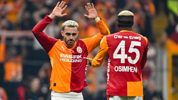 Galatasaray forması giyen iki futbolcu maç sırasında birbirine el sallıyor.