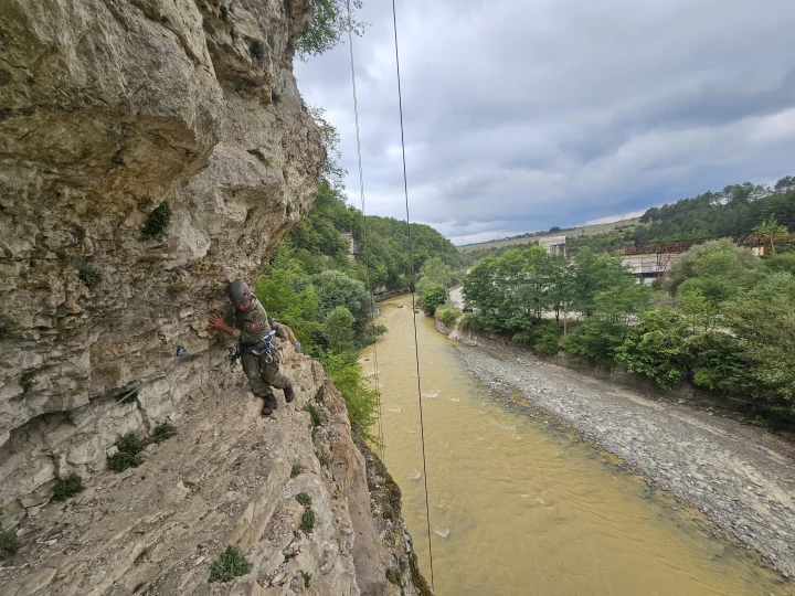Bir asker, kayalık bir yamaçta ip ve tırmanış ekipmanlarıyla ilerliyor