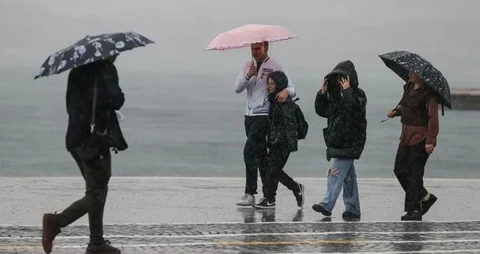 Yağmurlu havada sahil kenarında şemsiyeyle yürüyen kişiler