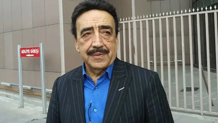 Hakkı Bulut, mavi gömlek ve koyu renk ceketle bir binanın önünde