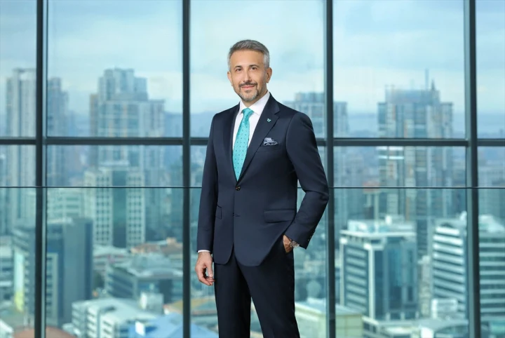 Hasan Ecesoy, cam cepheli bir ofiste takım elbiseyle ayakta duruyor.
