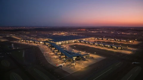 Alacakaranlıkta ışıklandırılmış bir havalimanı ve terminal çevresinde park etmiş uçaklar