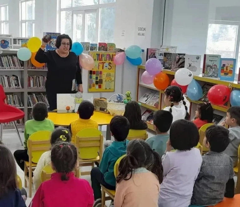 İlknur Artuğ, çocuklara kütüphanede kitap okuyor.