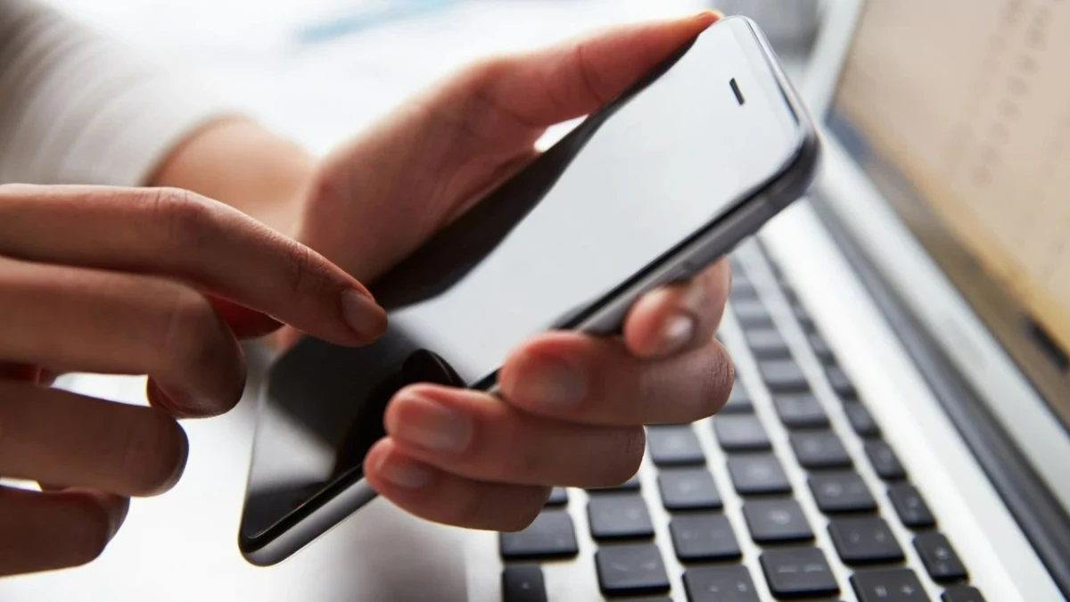 Bir kişinin elinde tuttuğu akıllı telefon ve arka planda bilgisayar klavyesi