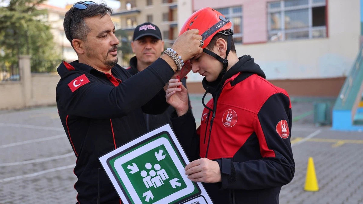 Arama kurtarma görevlisi öğrenciye kırmızı kask takıyor
