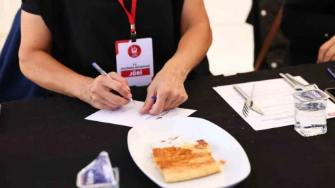Yemek yarışmasında jüri üyesi masadaki kete örneğini değerlendirirken not alıyor