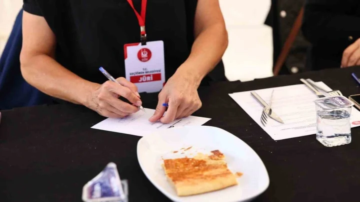 Yemek yarışmasında jüri üyesi masadaki kete örneğini değerlendirirken not alıyor