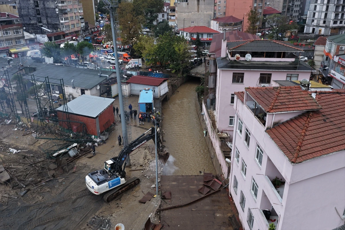 Yerleşim bölgesinde taşkın suyu ve çamur arasında çalışan iş makinesi görülüyor.