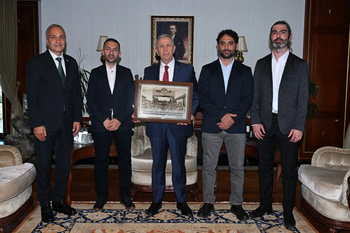 Mansur Yavaş ve beraberindeki heyet, ziyarette bir arada duruyor; Yavaş elinde çerçeveli bir tablo tutuyor.
