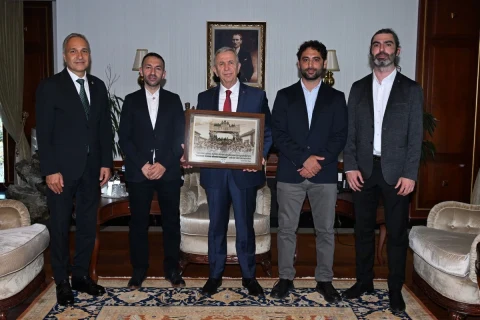 Mansur Yavaş ve beraberindeki heyet, ziyarette bir arada duruyor; Yavaş elinde çerçeveli bir tablo tutuyor.