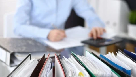 Evrak dosyaları önünde hesap makinesiyle çalışan bir kişi