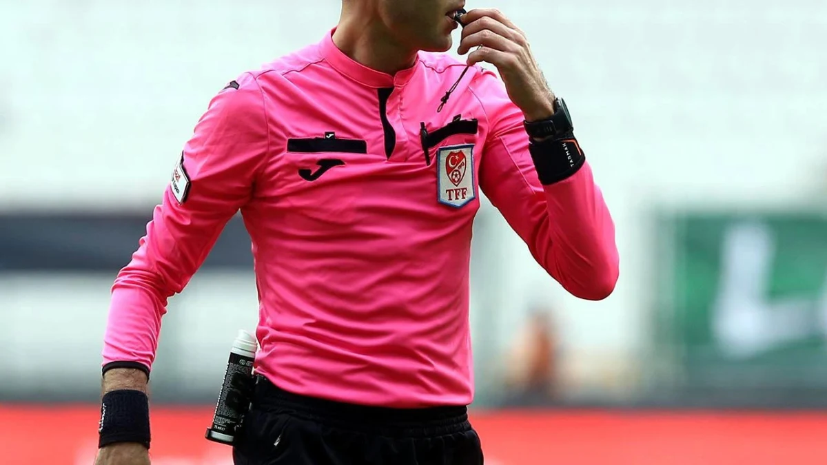 Pembe forma giyen bir futbol hakemi maç sırasında düdük çalıyor.
