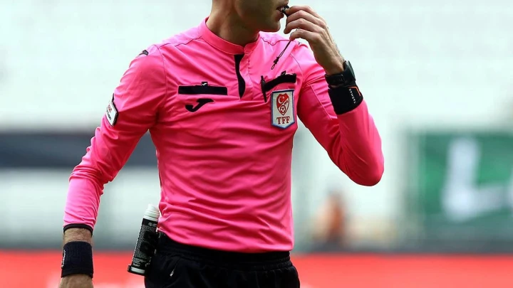 Pembe forma giyen bir futbol hakemi maç sırasında düdük çalıyor.