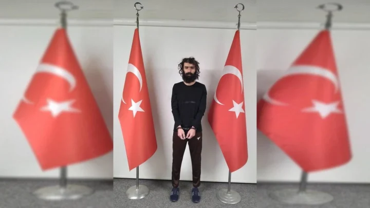 Türk bayraklarının önünde ayakta duran bir kişi