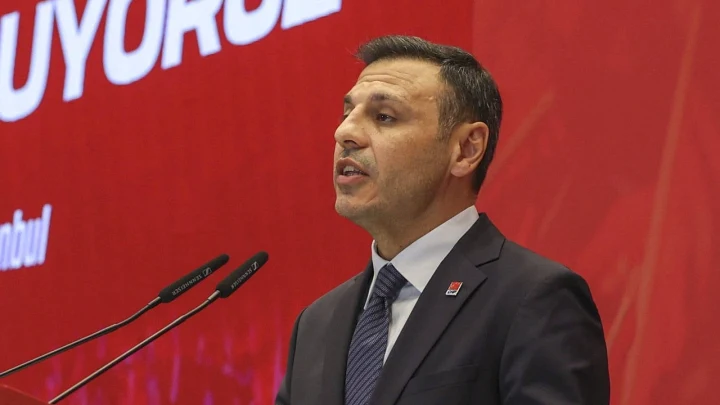 Özgür Çelik, kırmızı fon önünde mikrofonlarla konuşuyor