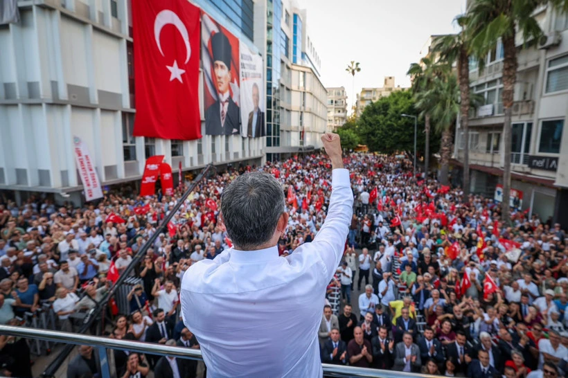 Özgür Özel, sahneden kalabalığa elini kaldırarak sesleniyor.