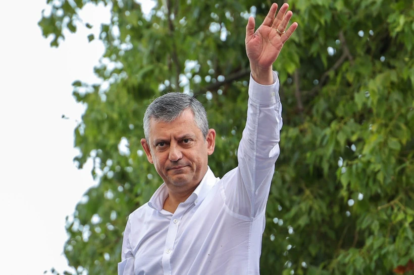 Özgür Özel, açık havada elini kaldırarak selam veriyor.