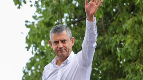 Özgür Özel, ağaçların önünde elini kaldırarak selam veriyor
