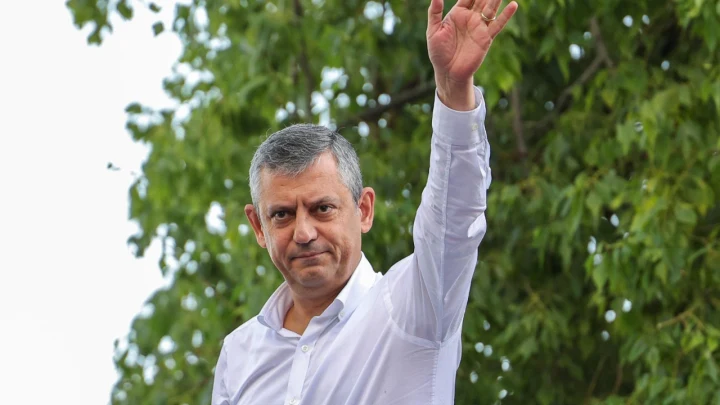 Özgür Özel, ağaçların önünde elini kaldırarak selam veriyor