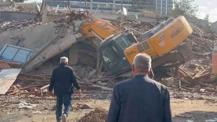 Yıkım alanında molozların arasında kalan sarı kepçe ve çevredeki görevliler