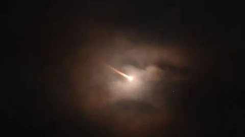Gece gökyüzünde ışık izi bırakan bir cisim ve çevresinde bulutlar