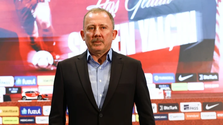 Sergen Yalçın, TFF ile imza töreninde takım arması önünde duruyor.