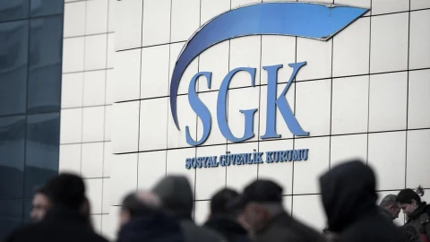 SGK binasının duvarındaki Sosyal Güvenlik Kurumu logosu ve ön planda insanlar