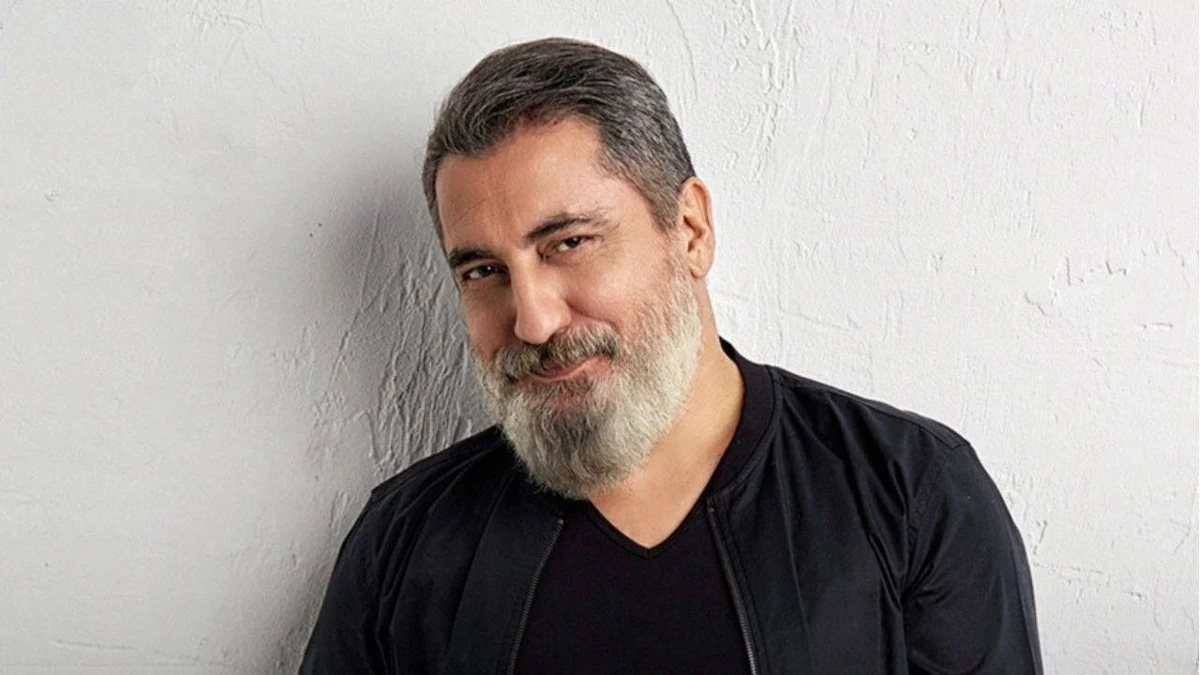Soner Olgun siyah tişört ve ceketle açık renk duvar önünde