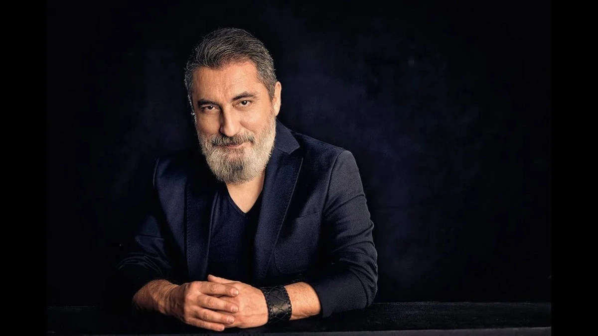 Soner Olgun koyu arka plan önünde masaya dayanmış halde