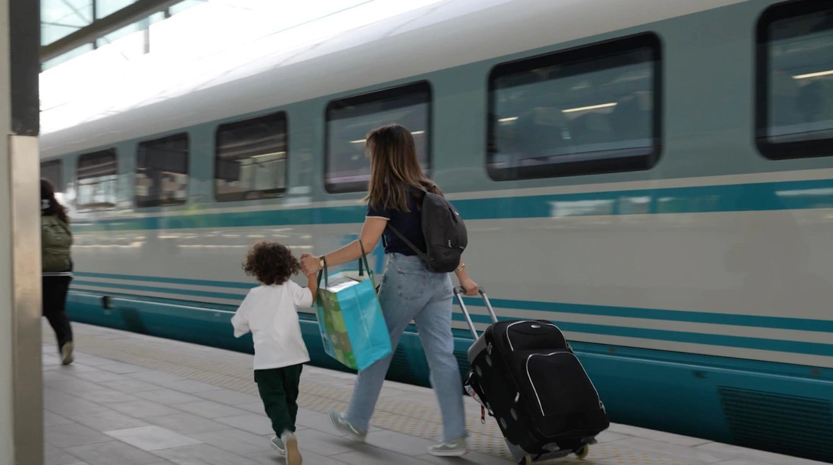 Peronda küçük bir çocukla birlikte valiz taşıyan yolcu ve tren