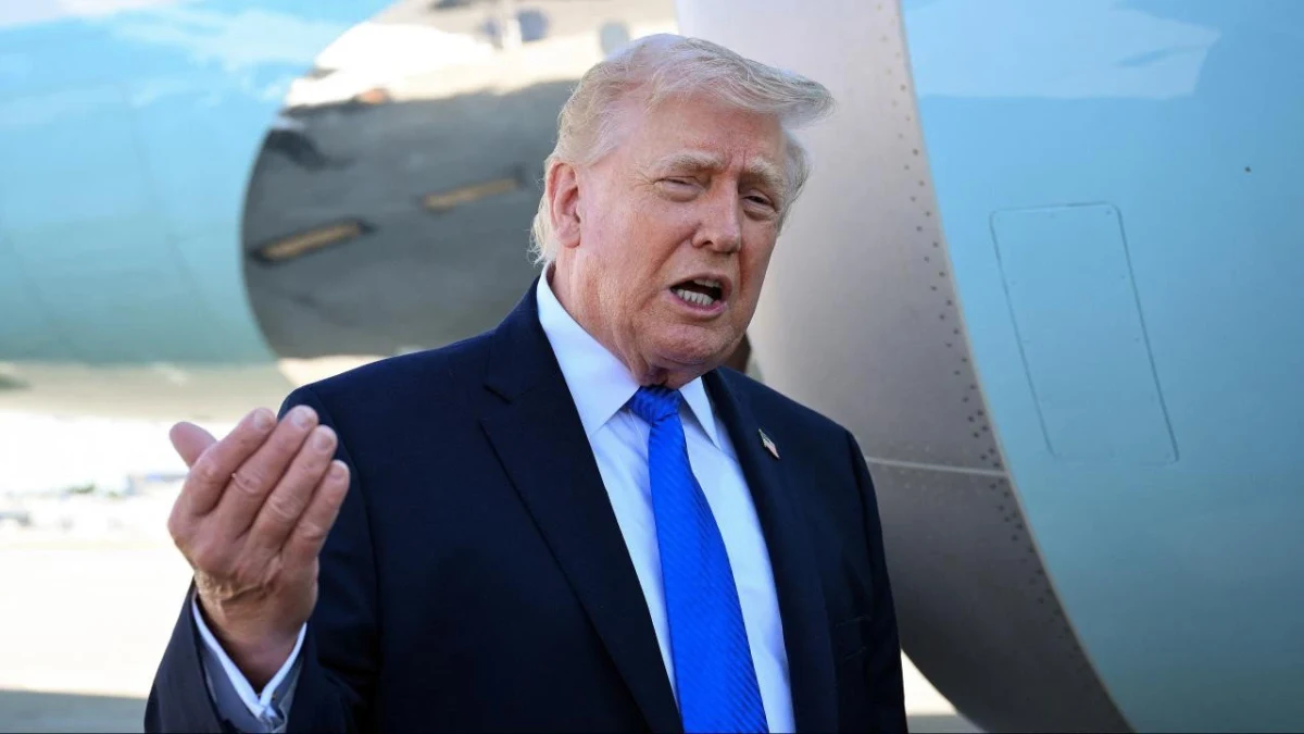 Donald Trump konuşurken elini kaldırıyor; arka planda bir uçak görülüyor.